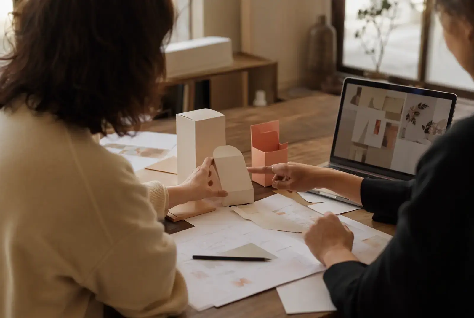 Two colleagues reviewing unbranded packaging prototypes together at a wooden table